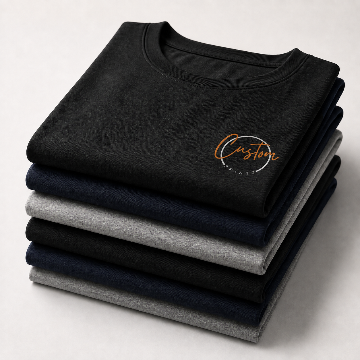 Stack of folded custom T-shirts in black, navy and grey with the Customprintz logo printed on the chest