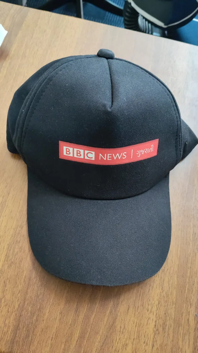 Black cap screen printed with the BBC News Gujarati logo