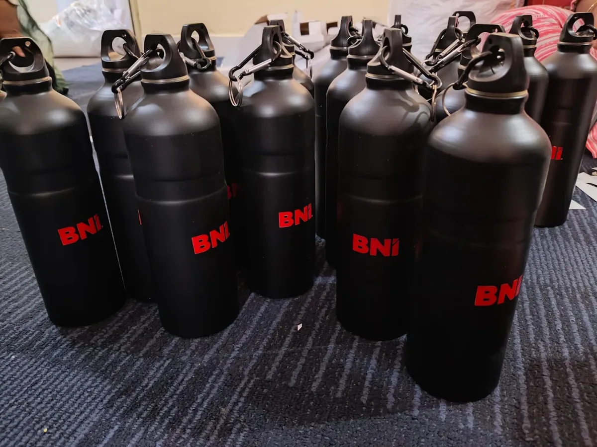 Matte black metal bottles with red BNI logos UV printed on the front, arranged in bulk