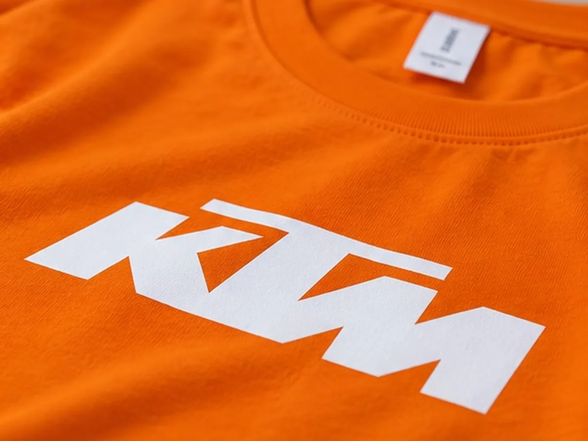 Close-up of the white screen printed KTM logo on the orange cotton T-shirt