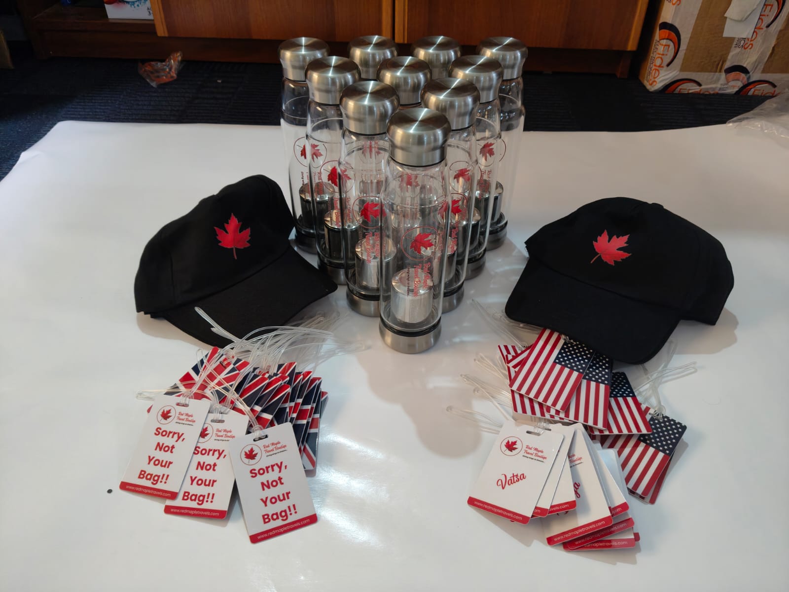 Red Maple Travel Boutique branded bottles, black caps and luggage tags arranged together